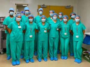 students wearing green scrubs, blue caps, and masks in hospital setting