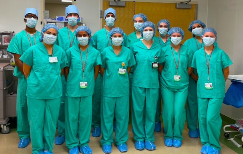 students wearing green scrubs, blue caps, and masks in hospital setting