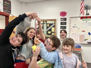 six students smiling together 3 of them are holding a tape measure