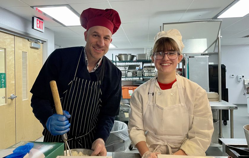 principal and student wearing chef uniforms make pasta