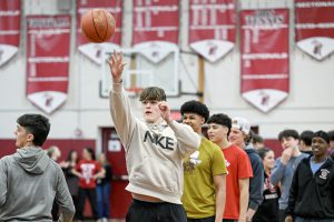 student shoots basketball and other watch behind him