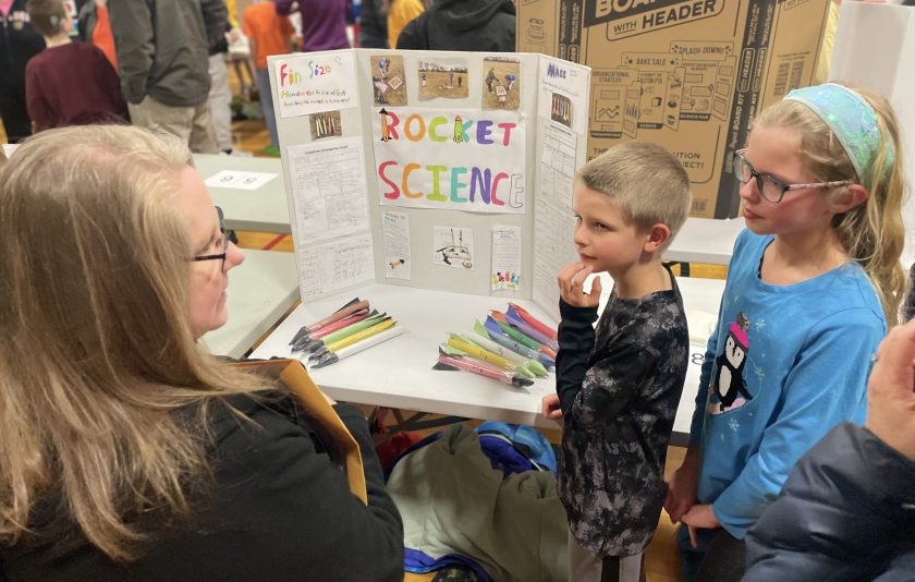 two students explaining science fair project to adult