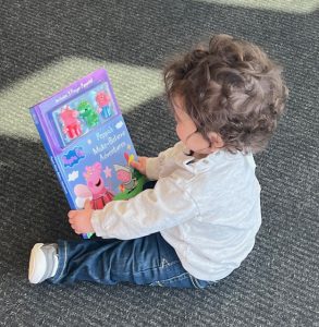 young child sits on floor holding a book about the size of the child