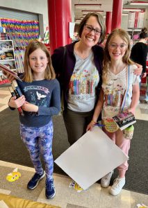 two students all smiles holding books with an adult standing between them