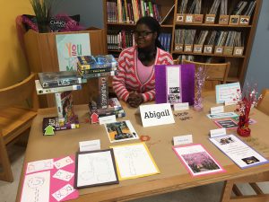 student sits behind a table with her poetry in different colorful forms